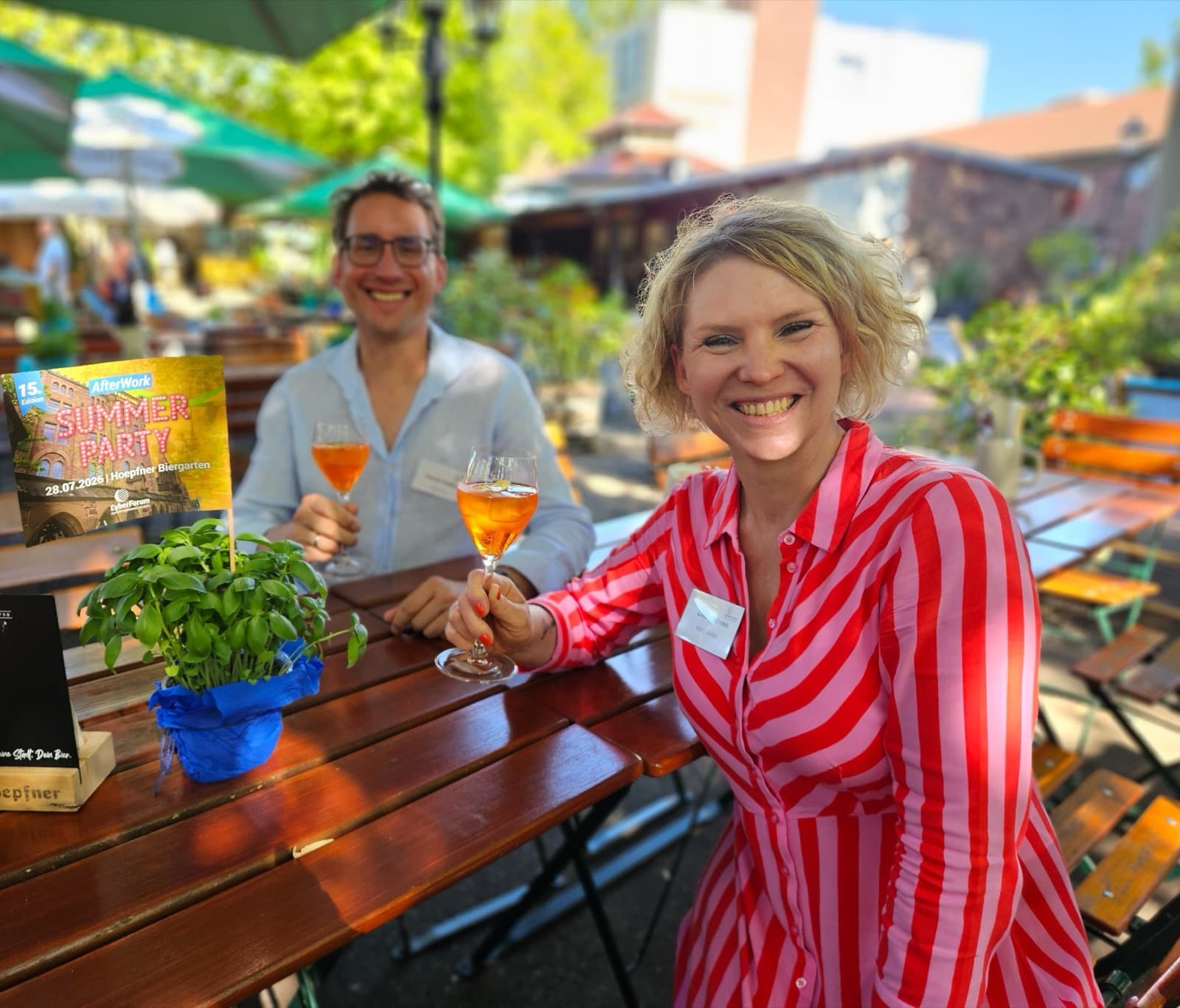Sascha and Linda raising a glass in a sunny beer garden at the CyberForum Summer Party