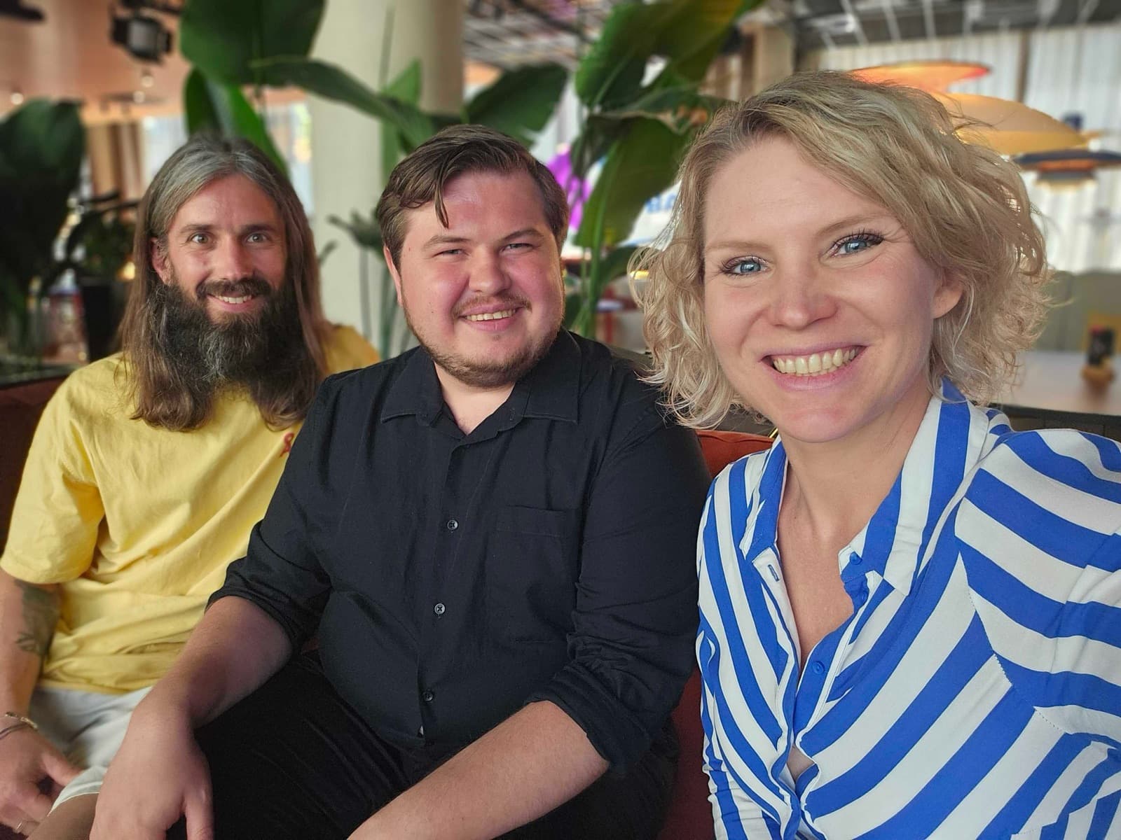 Jonas, Denys and Linda smiling on a bench seat in a restaurant